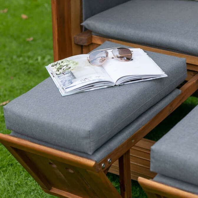 Strandkorb Fußstütze mit grauer Polsterauflage, darauf liegende Zeitschrift und Sonnenbrille im Garten