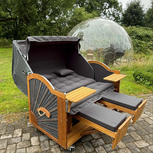 Strandkorb Prieß Modell Meister aus Iroko Holz mit dunkelgrauem PE Geflecht, abgebildet mit zwei ausziehbaren Fußstützen.