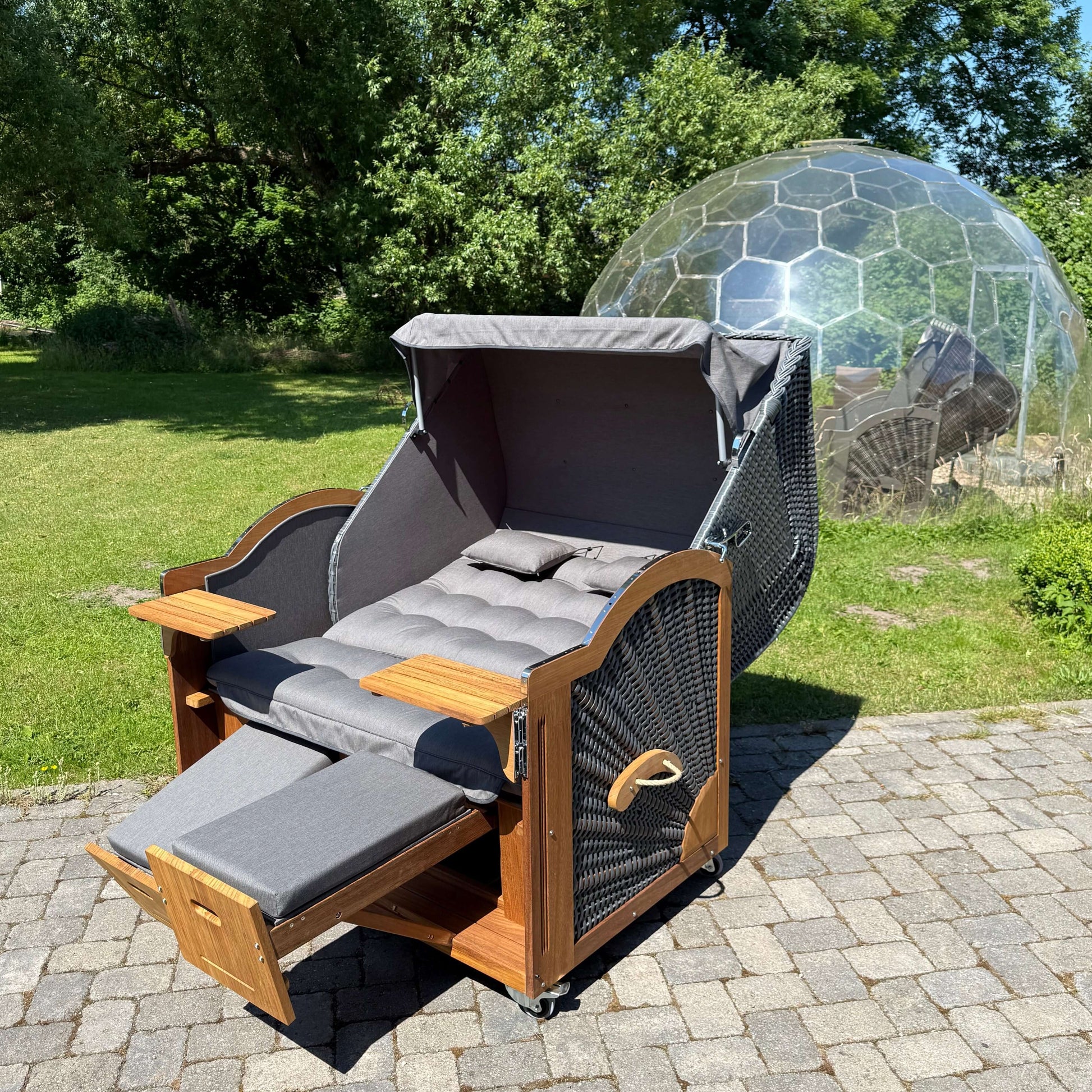 Strandkorb Prieß Modell Meister aus Iroko Holz, dunkelgrauem GEflecht und anthrazitfarbigem Stoff im Freien.