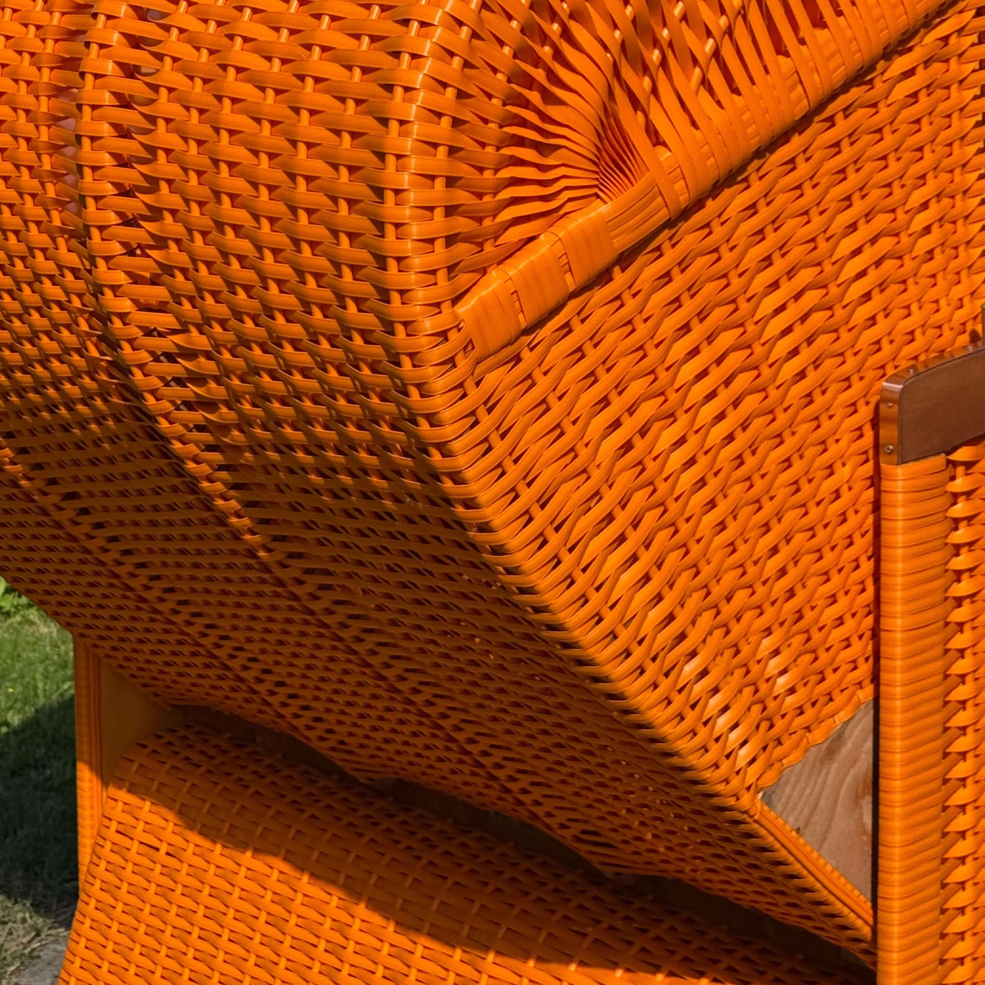 Detailansicht eines Strandkorbs in leuchtendem Orange, mit geflochtenem Material und Holzrahmen.