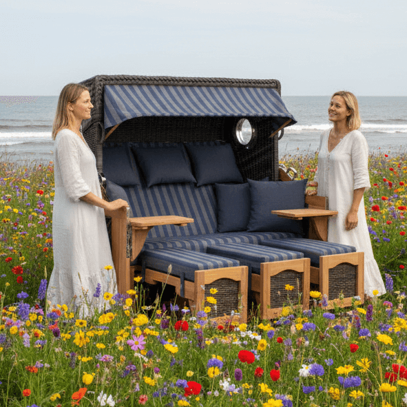 Strandkorb deVries PURE S Seemöwe Teak mit Bullaugen und blauen Polstern im Blumenfeld am Meer