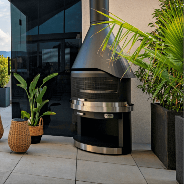 HermaPro Edelstahl Gartenkamin Vario mit gesteppter Haube auf moderner Terrasse neben Pflanzen