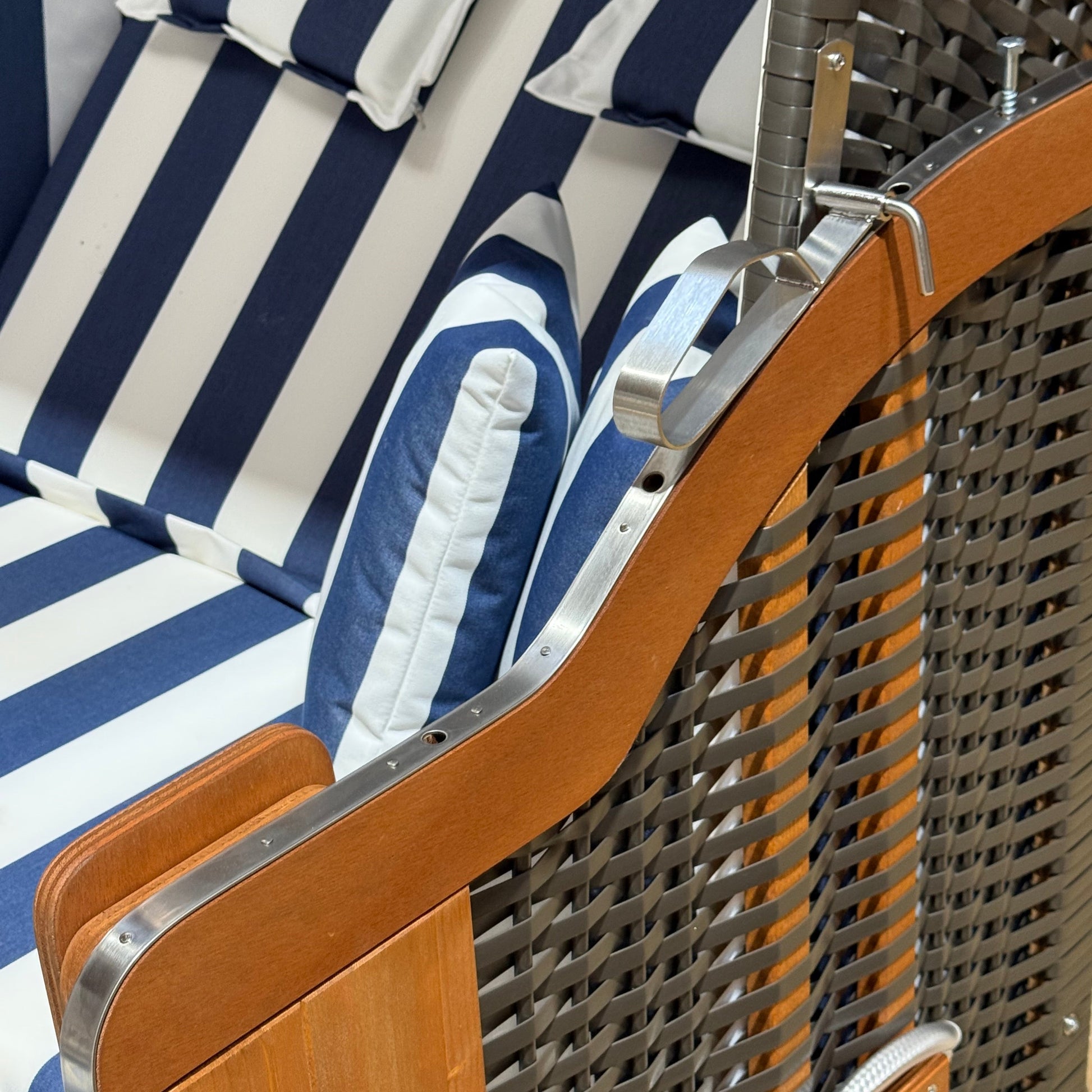 Detailaufnahme des Strandkorbs Kiel Edelstahl 250 Plus mit blau-weißem PVC-Geflecht und gepolsterten Kissen.