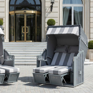 Zwei Strandkorb Sonnenpartner Modelle Classic PE-Geflecht in Onyx Farbe, Holz grau, vor einem eleganten Gebäude.