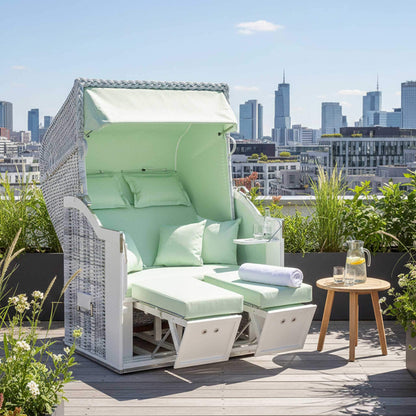 Strandkorb Classic 2-Sitzer white-washed mit hellgrünen Kissen auf einer Dachterrasse mit Stadtansicht.