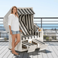 Strandkorb Sonnenpartner Classic weiss mit grau-weißen Streifen, Frau stehend daneben auf Terrasse mit Meerblick