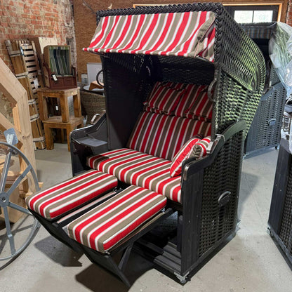 Strandkorb Kiel 255 Plus mit grauem Holz, anthrazitem PVC-Geflecht und gestreiften Kissen in rot und beige.