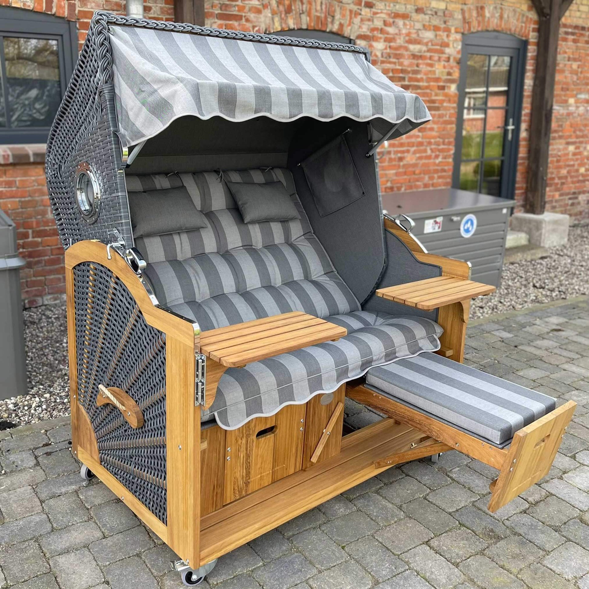 Strandkorb Prieß Modell Meister Iroko Holz mit anthrazit PE Geflecht und hellgrauem Dessin, bequeme Liegefläche.