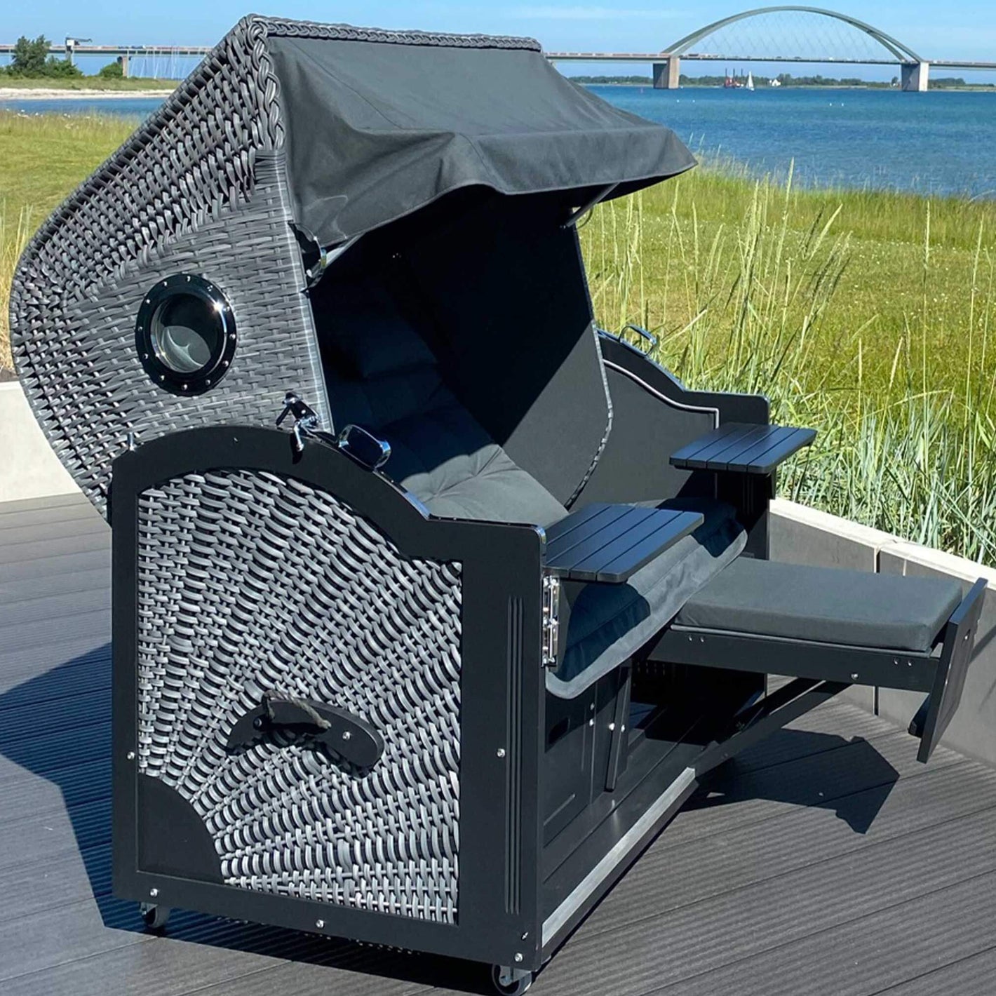 Strandkorb Prieß Modell Meister 7028 aus Lärche schwarz mit dunkelgrauem PE-Geflecht, verstellbare Fußstützen, am Wasser auf Terrasse