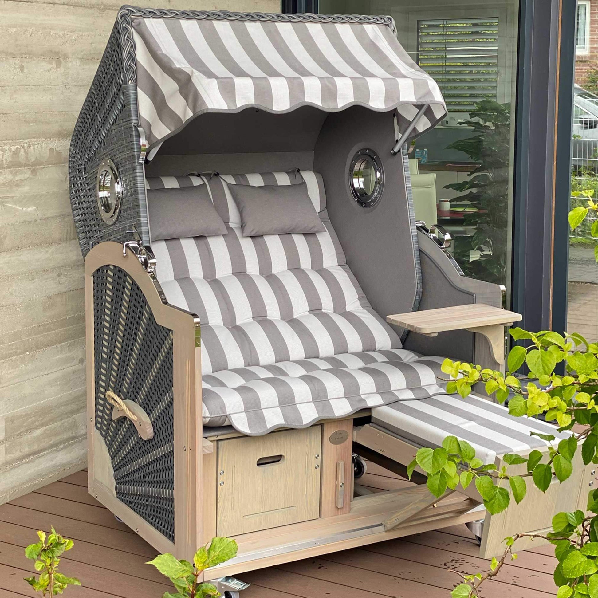 Strandkorb Prieß Modell Meister aus Lärche Vintage grau mit dunkelgrauem PE-Geflecht und Streifenpolster auf Terrasse