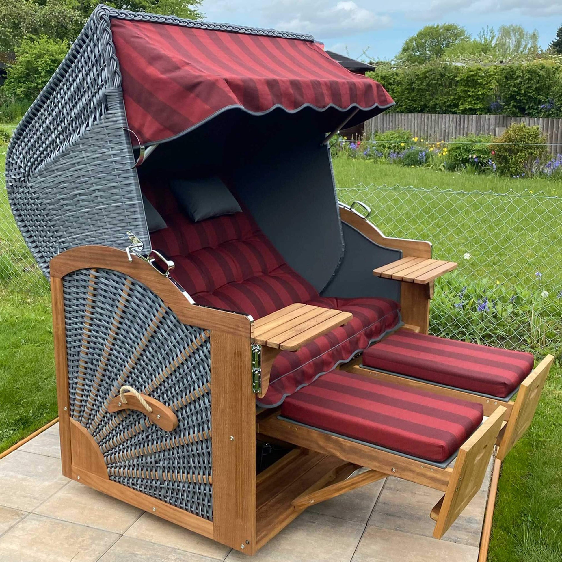 Strandkorb Prieß Modell Meister aus Iroko Holz mit dunkelgrauem PE Geflecht und rot gestreiftem Stoffdessin, im Außenbereich.