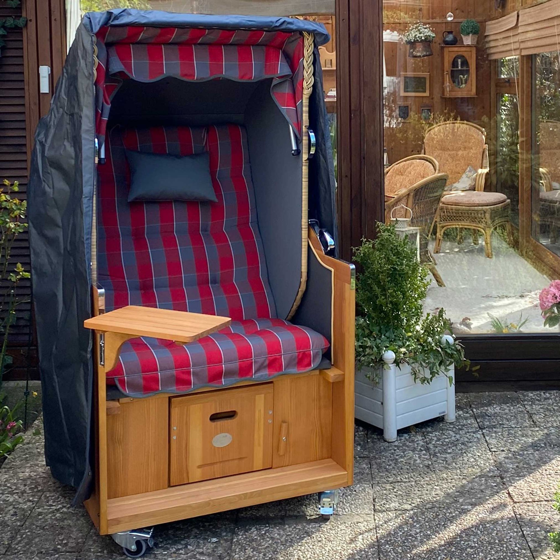 Strandkorb Prieß Modell Meister mit rot-kariertem Stoffdesign, Lärche Holz und klappbarem Tisch, ideal für entspannende Tage im Garten.