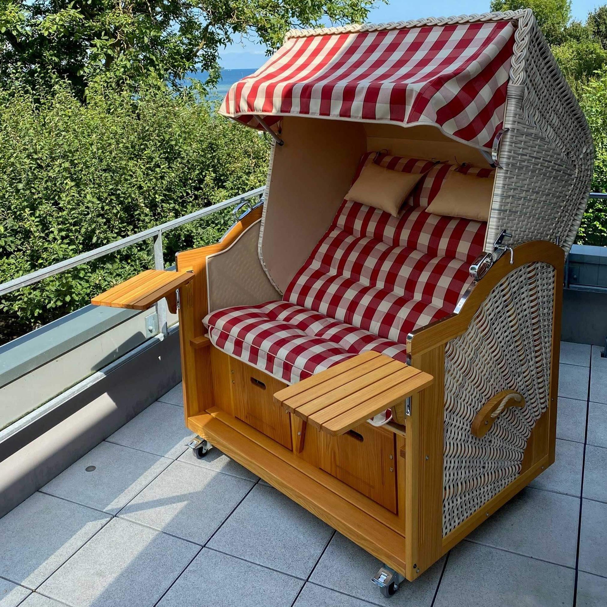 Strandkorb Prieß, Modell Meister mit Holz und PE-Geflecht, rot beige creme Stoff auf Balkon im Freien.