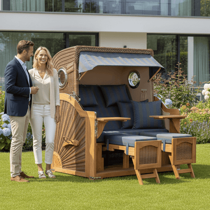 Strandkorb Düne Grande 2,5 Sitzer Teak PE banana mit Bullaugen und blau anthrazit Polstern im Garten mit Paar