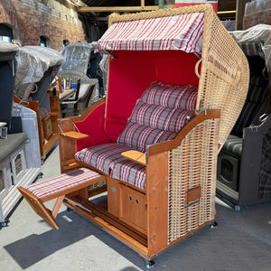 Strandkorb Sonnenpartner Modell Classic mit rot-gestreiftem Sitzkissen, Holz lasiert, ideal für Strand und Garten.