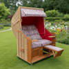 Strandkorb Sonnenpartner Modell Classic in rot mit Holz lasiertem Gestell in einer blühenden Gartenlandschaft.