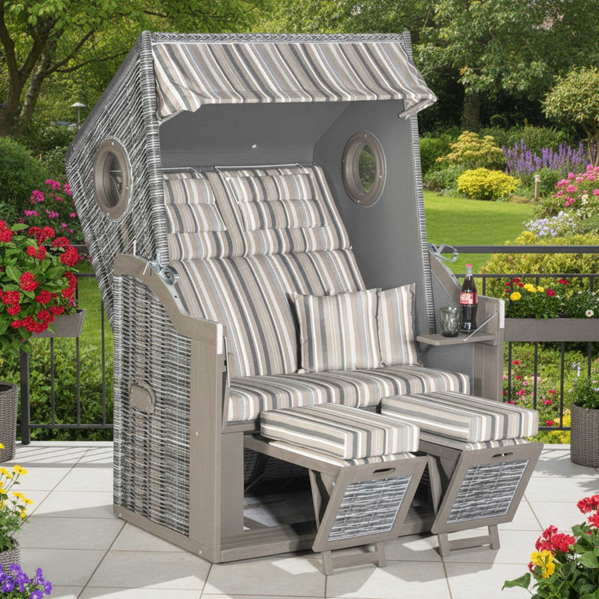 Strandkorb Rustikal 34 Z Bullauge aus grauem Pinienholz mit PE-Geflecht und gestreiften Kissen im Garten.