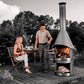 HermaPro Edelstahl Gartenkamin Vario mit glatter Haube auf Terrasse, Paar grillt und genießt Feuer im hochwertigen Gartenkamin