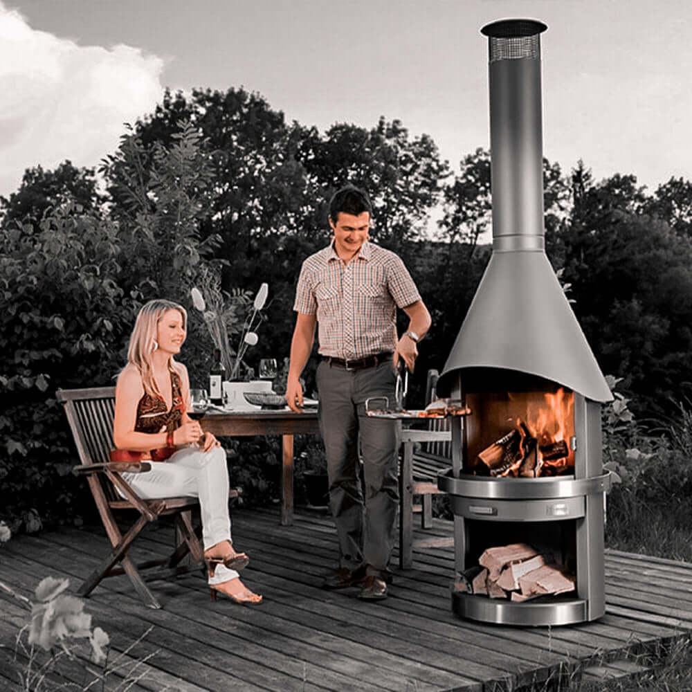 HermaPro Edelstahl Gartenkamin Vario mit glatter Haube auf Terrasse, Paar grillt und genießt Feuer im hochwertigen Gartenkamin