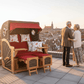 Strandkorb deVries PURE Seemöwe Teak PE stone grey auf Dachterrasse mit älterem Paar und Stadtblick bei Sonnenuntergang