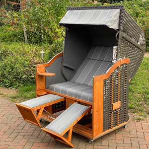 Strandkorb Sonnenpartner Modell Classic im anthrazit Geflecht mit Holzrahmen und grau meliertem Innenstoff, ausgestattet mit Klapptischen und Fußstützen.