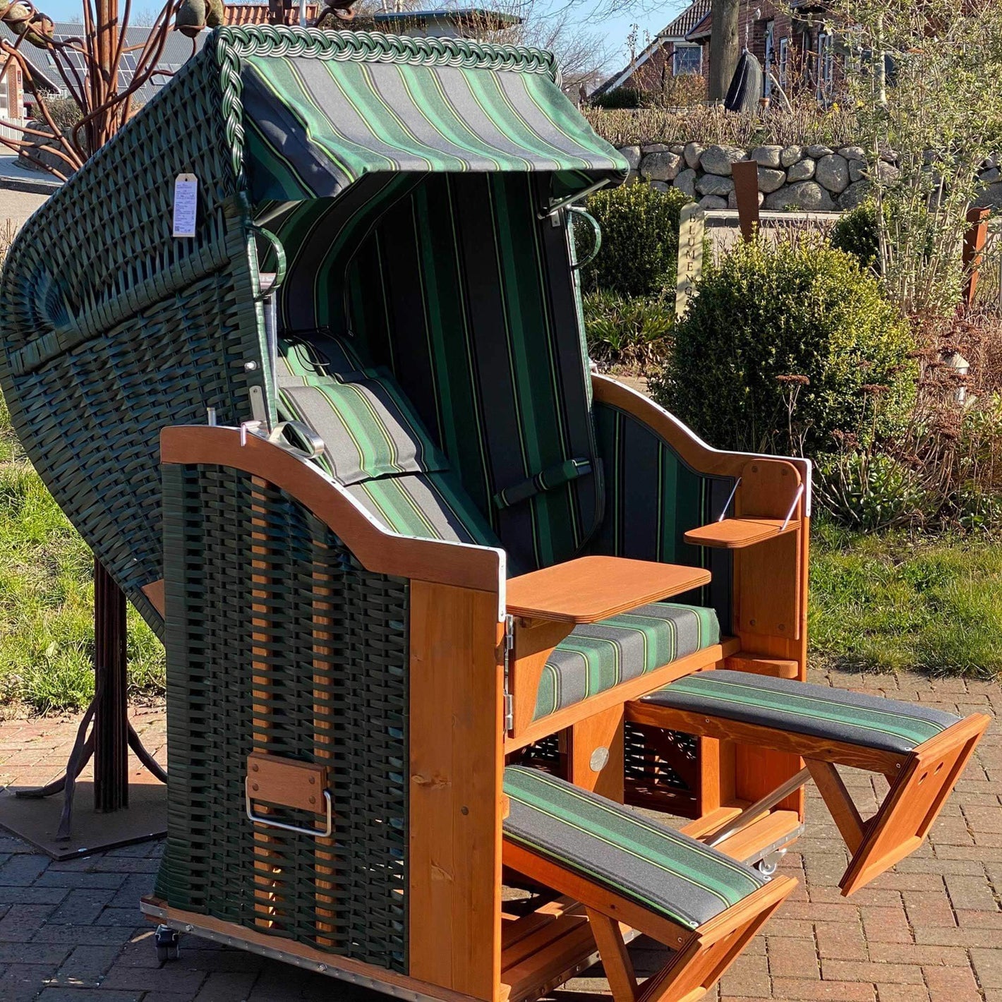 Strandkorb Sonnenpartner Modell Classic mit grünem Geflecht und Holz lasiert, ausgestattet mit Fahrrollen und Kopfkissen.