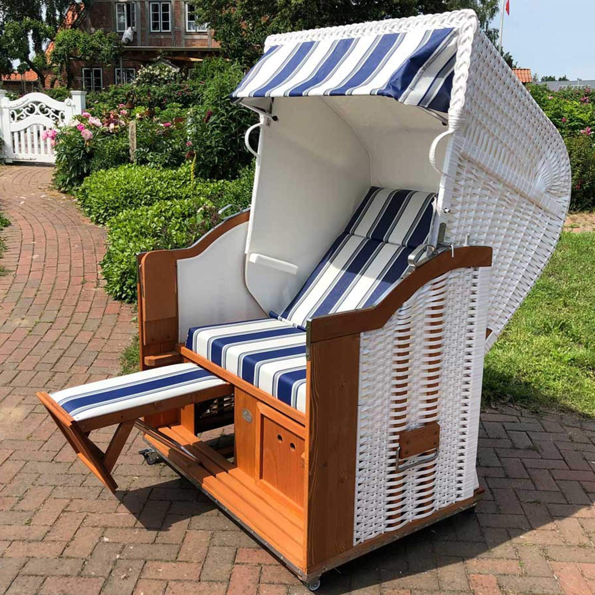 Strandkorb Sonnenpartner Classic weißes Geflecht mit blau grau weißen Streifen, Holz lasiert, Fahrrollen und Fußstützen im Garten