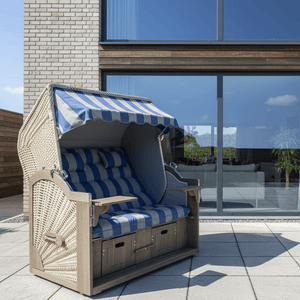 Strandkorb Prieß Modell Meister Vintage grau mit blau-weißem Bezug auf Terrasse vor moderner Hausfassade