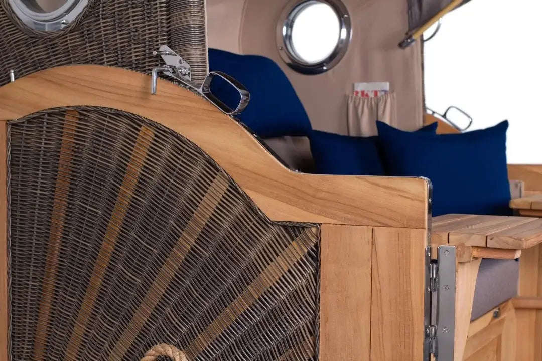 Strandkorb Baltikum Bullauge Teak PE Grey XL mit blauen Kissen und Holzdetails für den Garten.