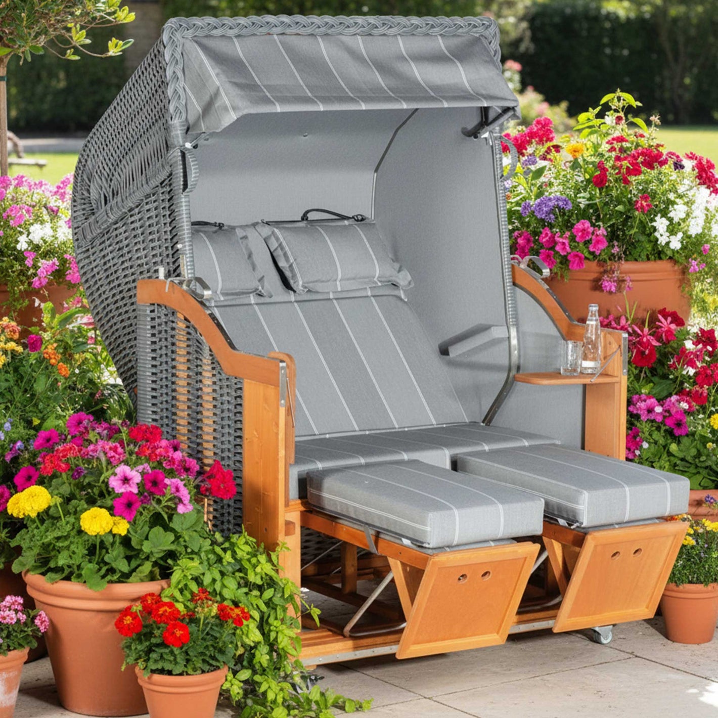 Strandkorb Sonnenpartner Classic PE onix grau mit Fahrrollen und Komfortkopfkissen im Garten, umgeben von bunten Blumen
