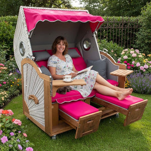 Strandkorb Prieß Modell Meister aus Iroko-Holz mit taupefarbenem PE-Geflecht und pinken Polstern im Garten