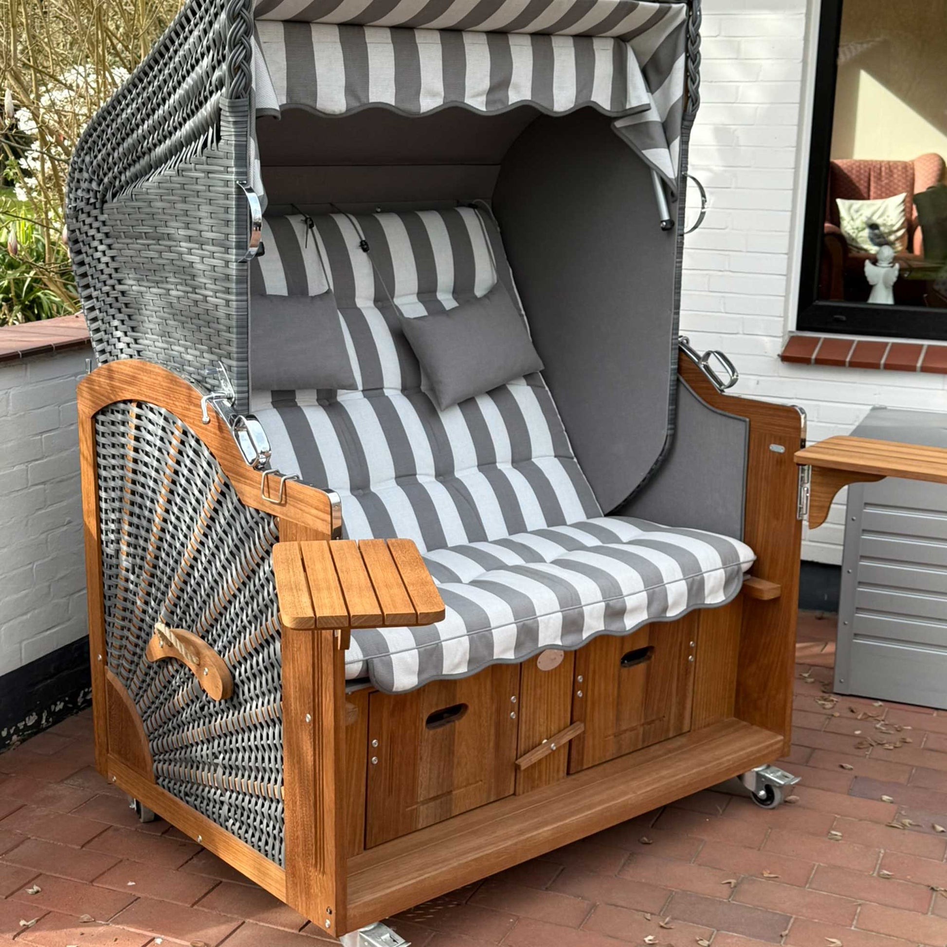 Strandkorb Prieß Modell Meister A106 aus Iroko Holz mit anthrazit PE-Geflecht und grau-weiß gestreifter Polsterung auf Terrasse