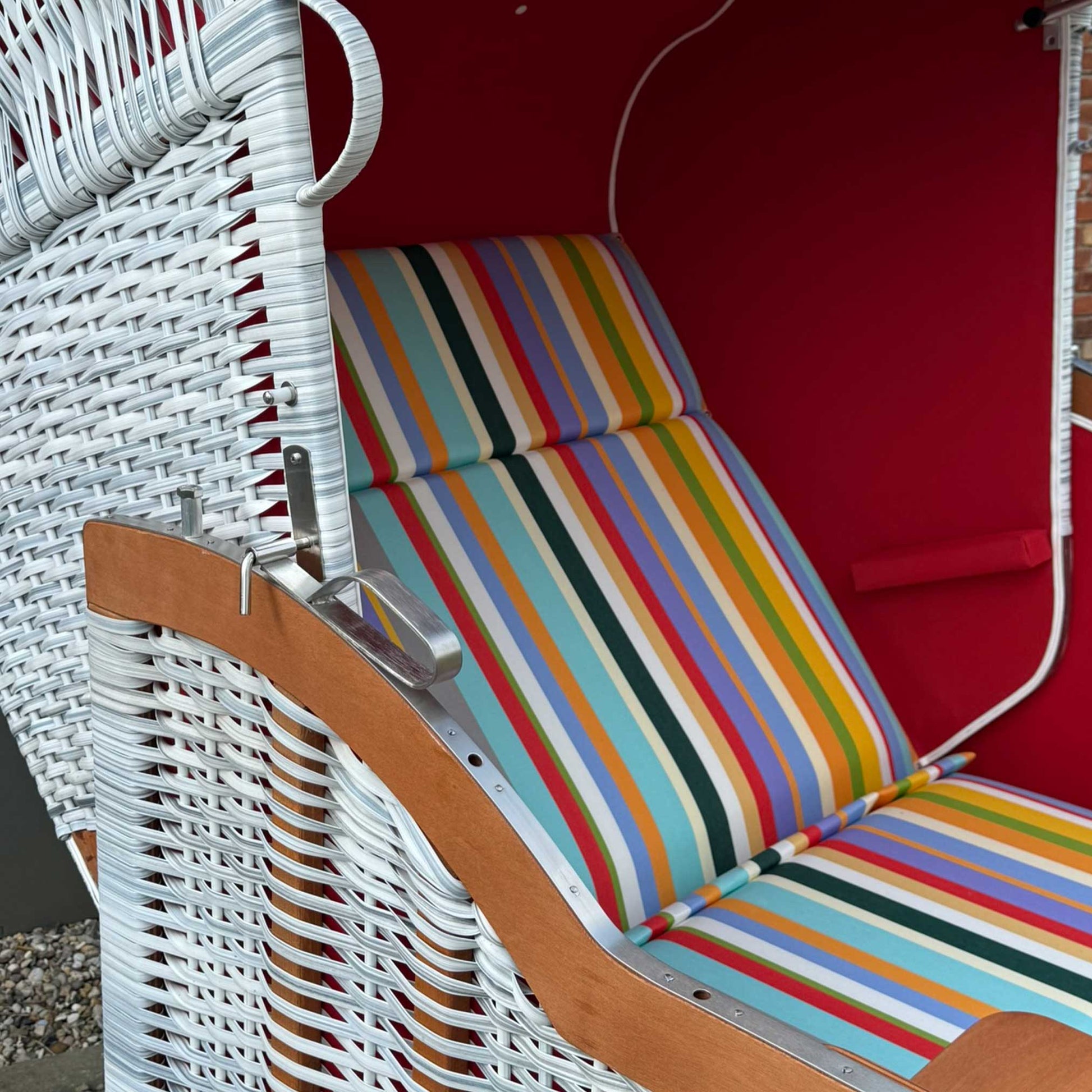 Strandkorb Sonnenpartner Modell Classic in weiß lasiert mit buntem Streifenmuster auf Sitzpolster.