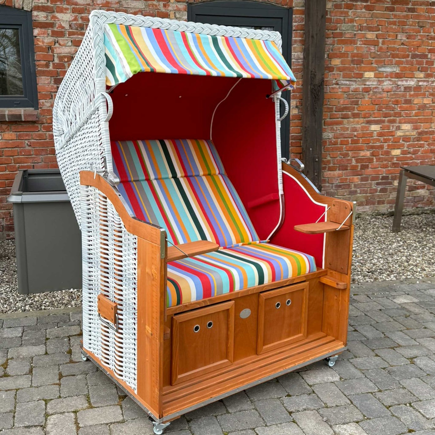 Strandkorb Sonnenpartner Modell Classic, weiß lasiert mit bunten Streifen in rot und weiß, ideal für Garten oder Terrasse.