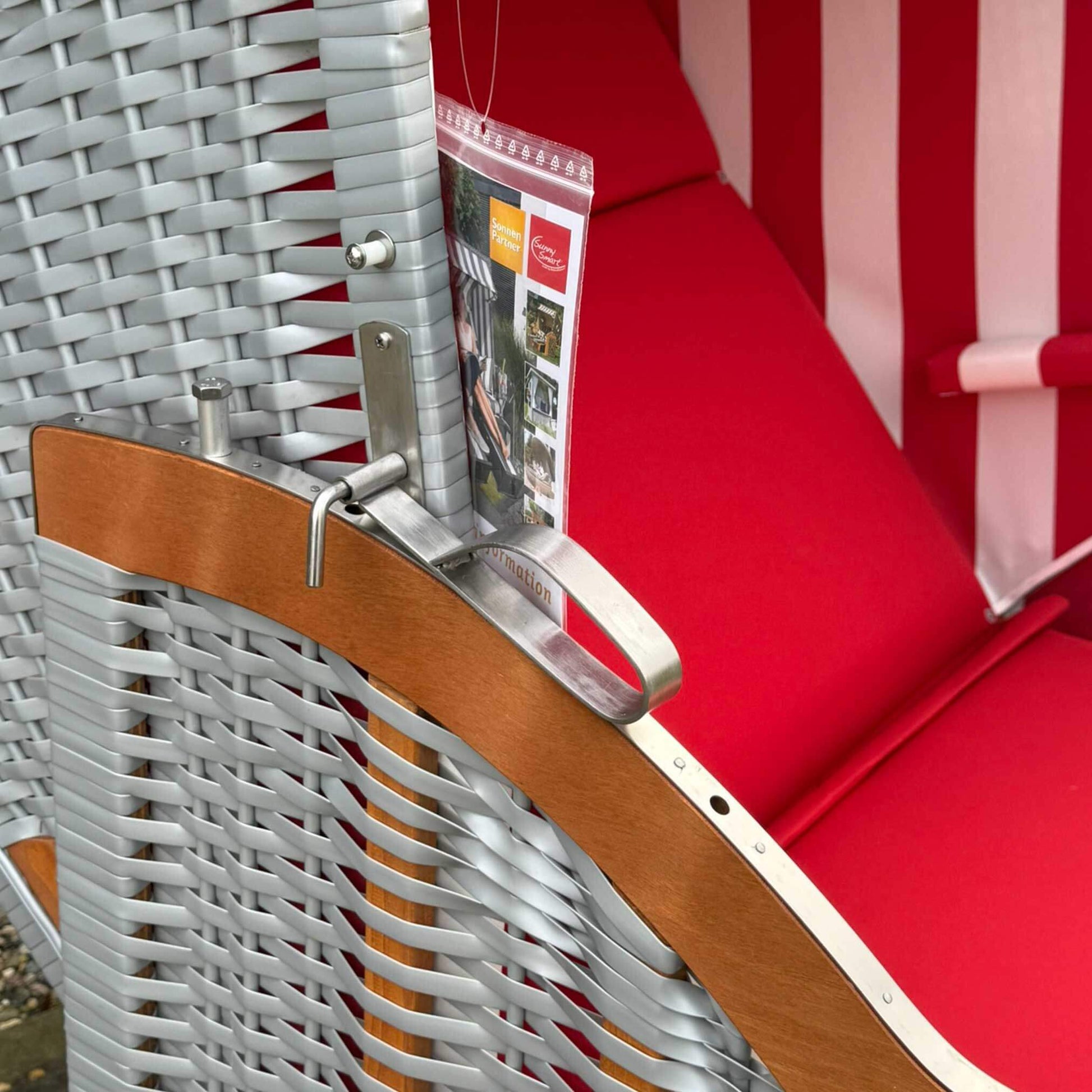 Detailaufnahme vom Strandkorb Sonnenpartner Classic rot weiß mit rotem Polster und Holzarmlehne.