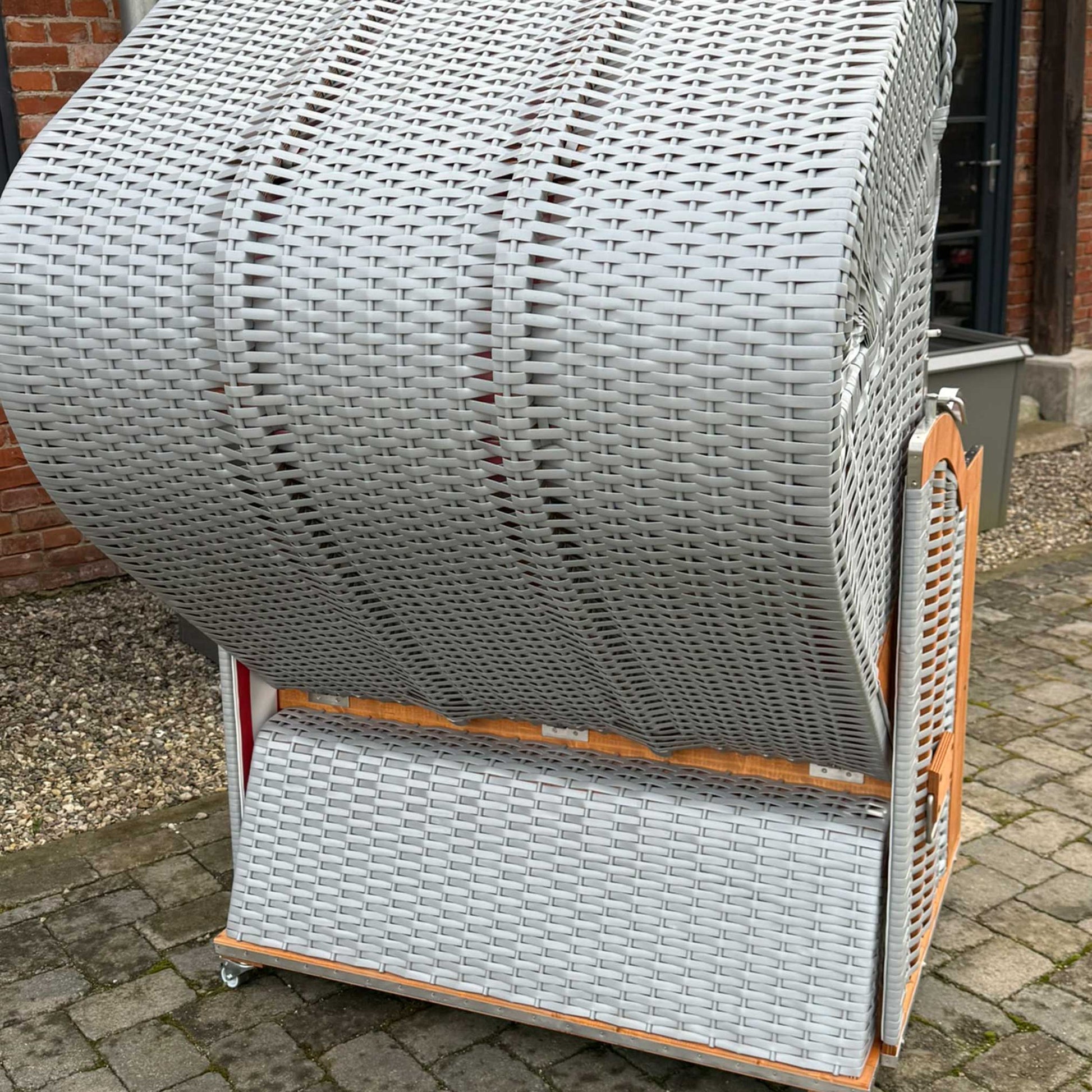 Strandkorb Sonnenpartner Classic rot weiß auf einem gepflasterten Boden, stilvolles Design in Grau, ideal für sonnige Tage.