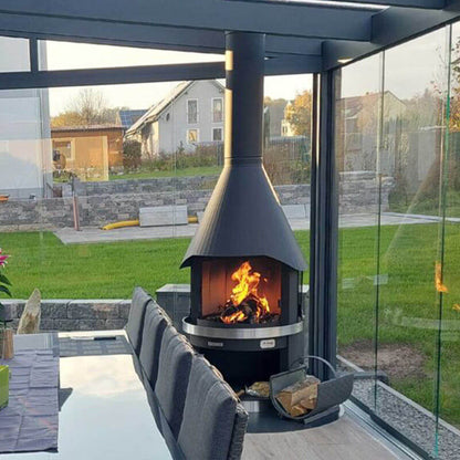 HermaPro Edelstahl Gartenkamin im modernen Wintergarten mit brennendem Feuer und gesteppter Haube als Grill und Kamin einsetzbar